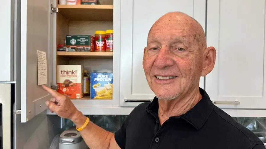 smiling man, keith monda, points to a Post-It note on a cabinet door