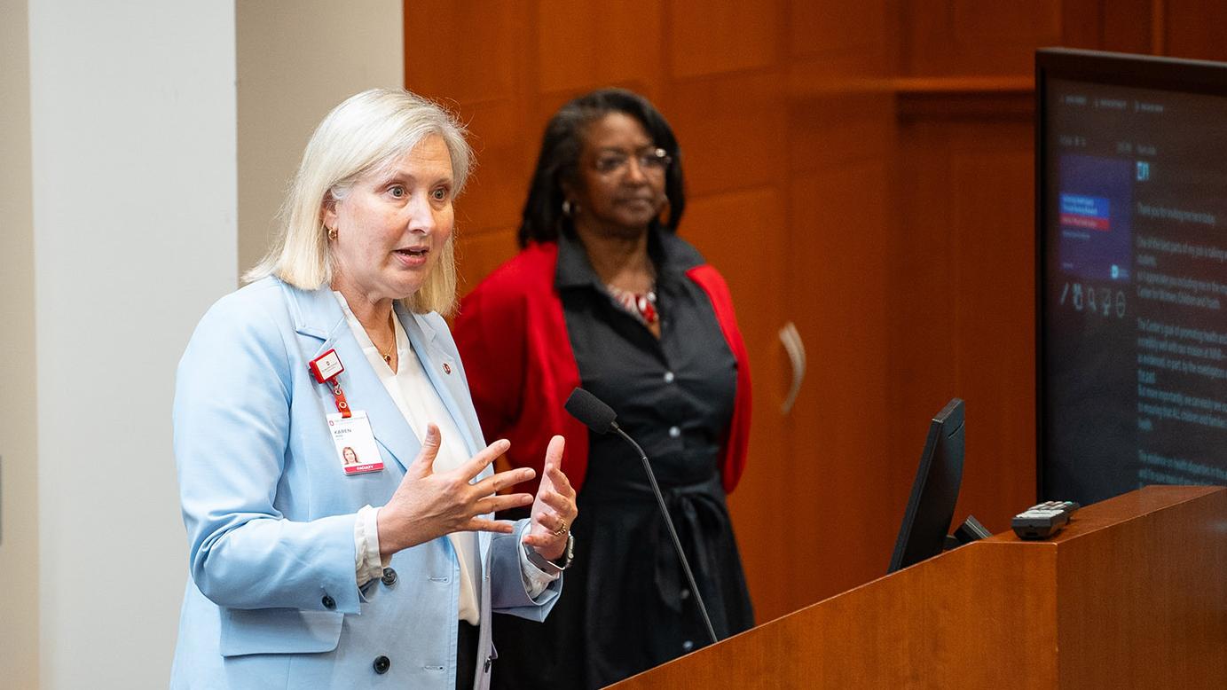 blonde-haired woman speaking to an audience at an event