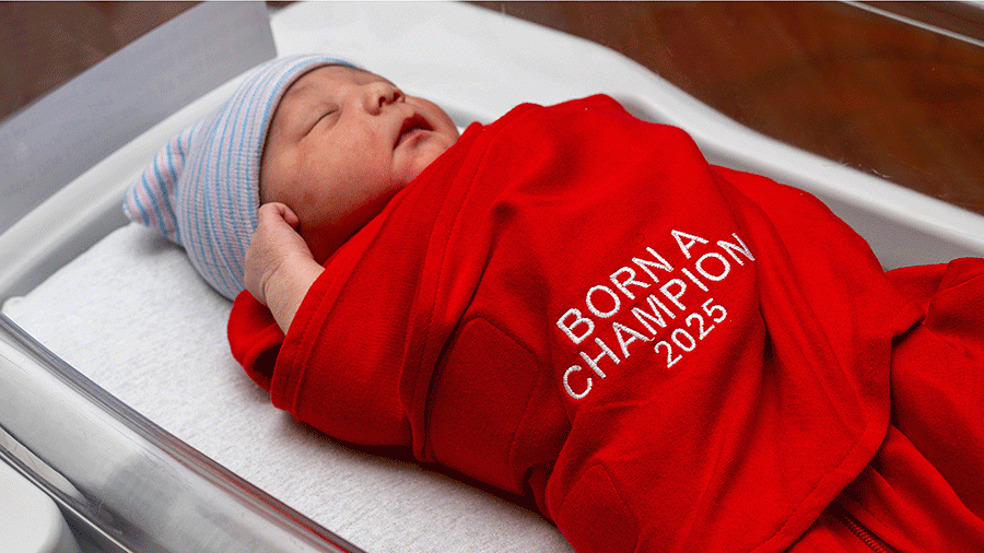 Newborn baby wrapped in a blanket with text that says Born a Champion 2025