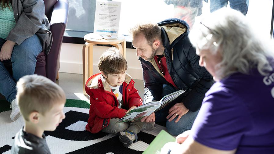 Children and adults sit on the floor reading books at Second Saturday Kids’ Day at WOSU.