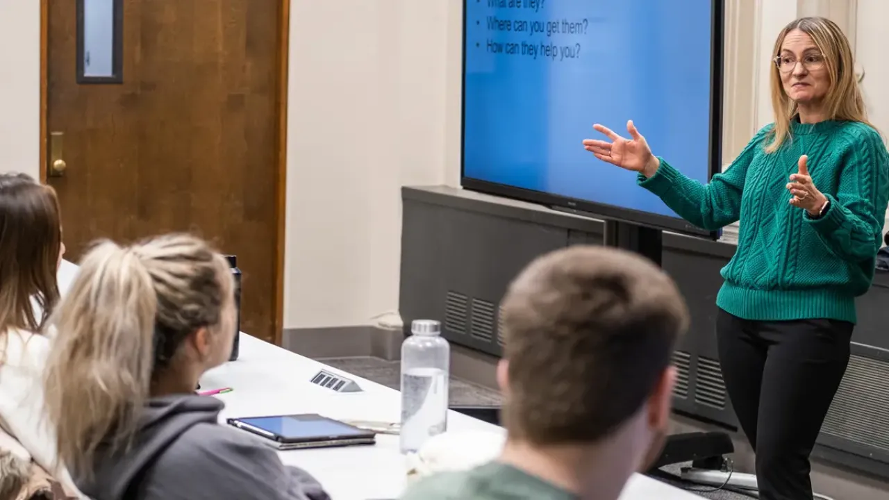 a woman wearing a green sweater gives a lecture to a room full of students
