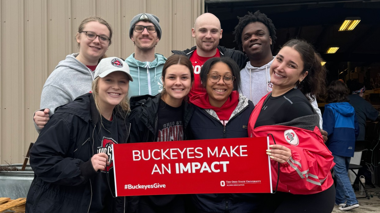 eight buckeye volunteers holding a scarlet sign that reads 'buckeyes make an impact'