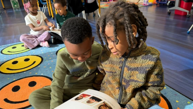 Kindergarten students sitting and reading together on the floor in a classroom.